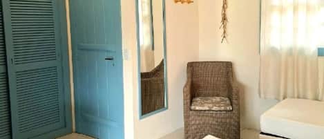 Una habitación con una puerta azul, un sillón de mimbre, un sofá blanco y un espejo en la pared.