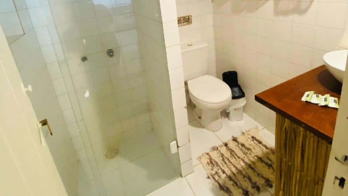A bathroom with a glass shower enclosure, a toilet, and a sink area with a rug.