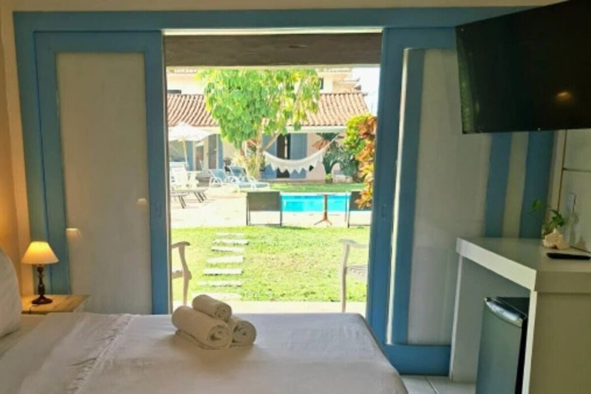 A hotel room with a bed, a TV, a desk, and a view of a pool and outdoor seating.