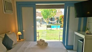 A hotel room with a bed, a TV, a desk, and a view of a pool and outdoor seating. - POUSADA DOS PÁSSAROS (Rio de Janeiro)