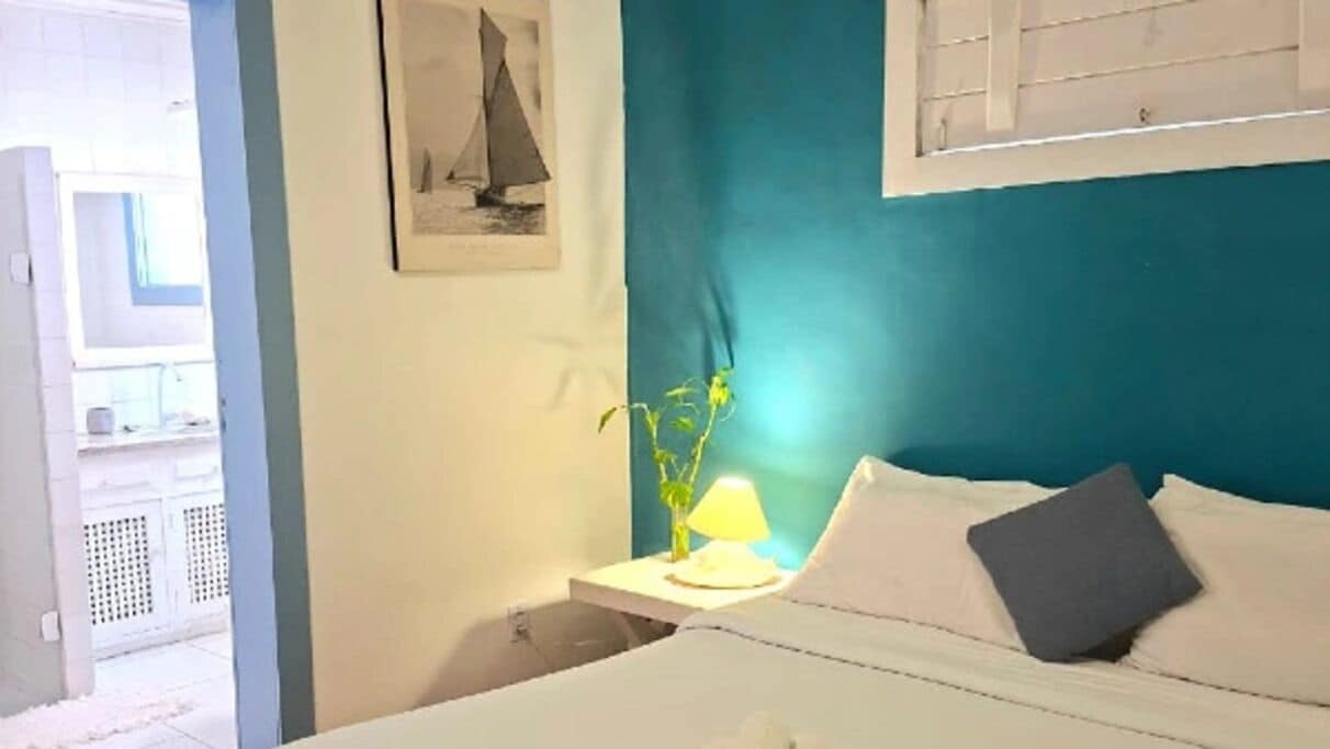 A bedroom with a bed, a nightstand with a lamp, a framed picture on the wall, and a window with blinds.