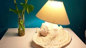 Una lámpara con pantalla cónica y base de concha marina, ubicada sobre una mesa junto a un florero transparente con una planta.