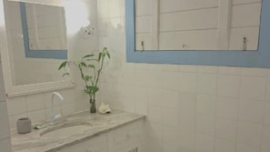 Un baño con lavamanos, espejo y una planta en maceta.
