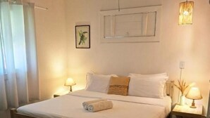 A bedroom with a wooden bed, two bedside tables with lamps, a window with curtains, and a wall-mounted picture. - POUSADA DOS PÁSSAROS (Rio de Janeiro)