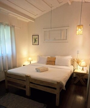 A bedroom with a wooden bed, two bedside tables with lamps, a window with curtains, and a wall-mounted picture. - POUSADA DOS PÁSSAROS (Rio de Janeiro)