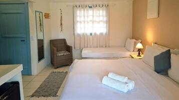 A hotel room with two beds, a chair, a desk, and a window with curtains.