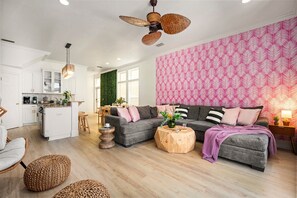 Una sala de estar moderna con un sofá gris, una mesa de centro de madera y un comedor con una pared verde y armarios blancos.