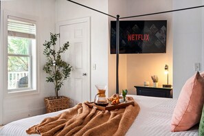 A bedroom with a bed, a wall-mounted TV displaying the Netflix logo, a bedside table with a lamp, and a window with blinds. - MilSViewsI PoolI BarrelSaunaIGulf ViewsI25Steps2BeachIGame RoomIPCB Beachlife (Panama City Beach)