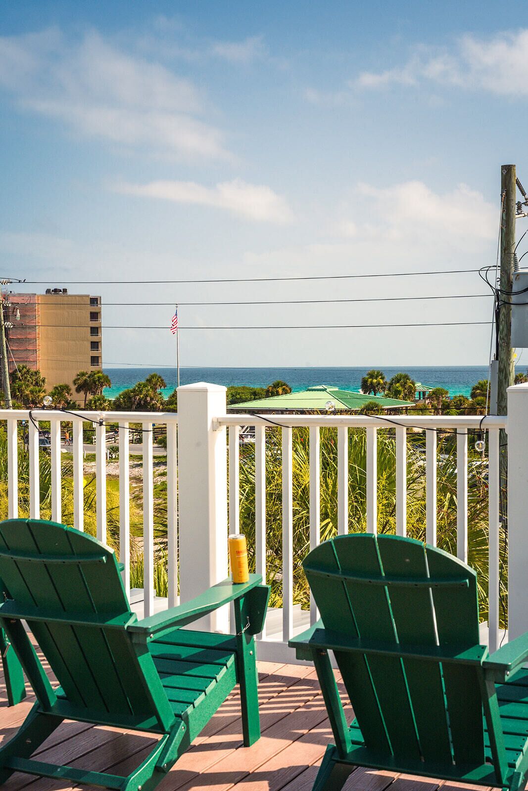 A balcony with two green Adirondack chairs, a white railing, and a view of the ocean.