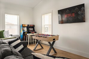 A living room with a foosball table, two arcade games, a sofa, and a wall-mounted TV displaying the Netflix logo. - MilSViewsI PoolI BarrelSaunaIGulf ViewsI25Steps2BeachIGame RoomIPCB Beachlife (Panama City Beach)