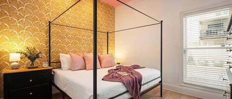 A four-poster bed with a white and pink bedding set, a bedside table with a lamp, and a wall with a leaf pattern.