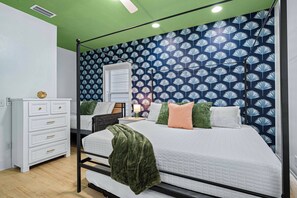 A bedroom with a four-poster bed, a dresser with drawers, a bedside table with a lamp, and a wall with a leaf pattern. - MilSViewsI PoolI BarrelSaunaIGulf ViewsI25Steps2BeachIGame RoomIPCB Beachlife (Panama City Beach)