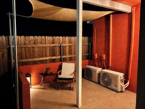 A patio area with a wooden fence, a table with a chair, and two air conditioning units.
