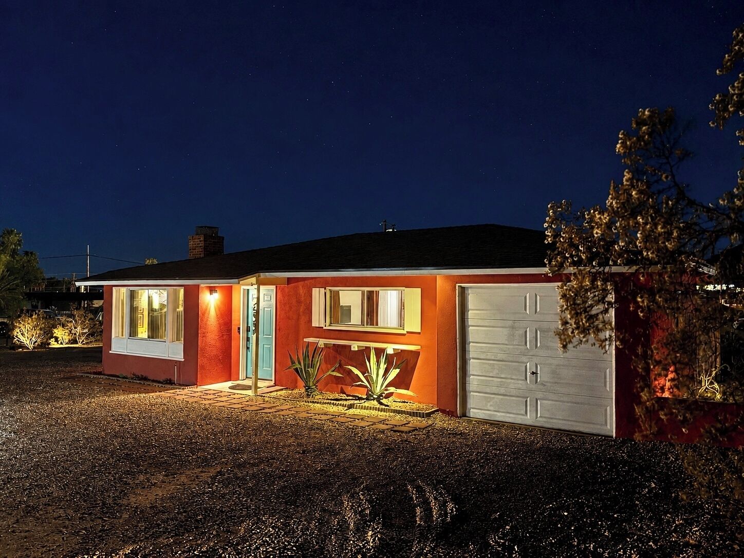 A single-story house with a garage, a front door, and a small porch area with plants.
