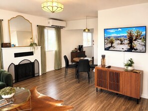 A modern living room with a fireplace, dining area, and a mounted TV displaying a desert landscape.