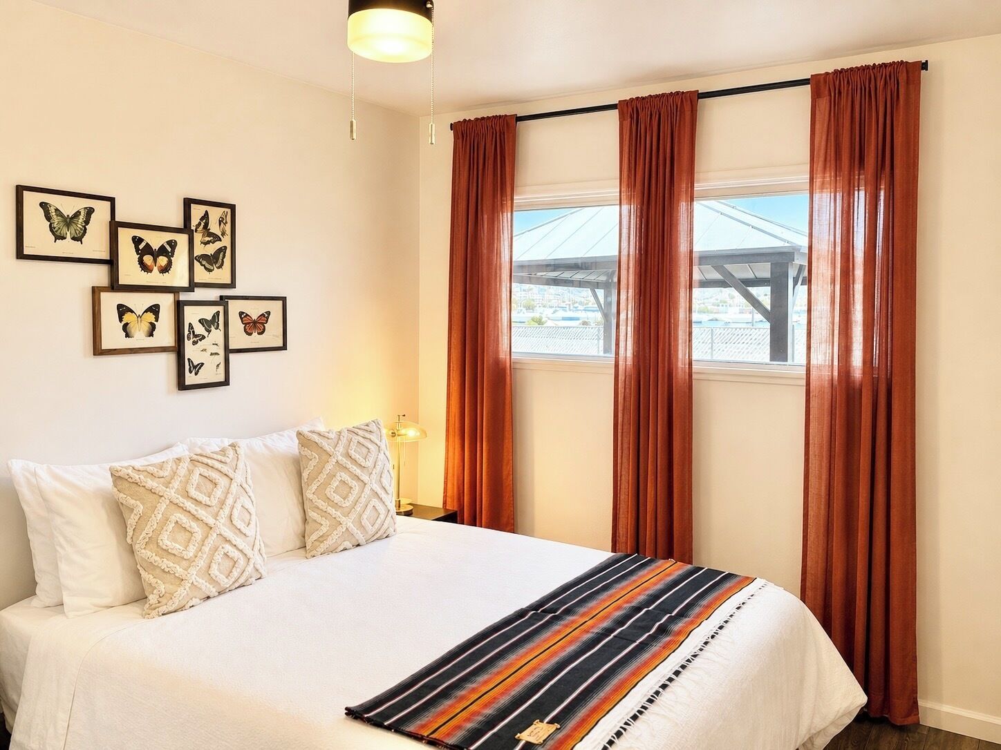 A hotel room with a bed, a window with curtains, and butterfly wall art.