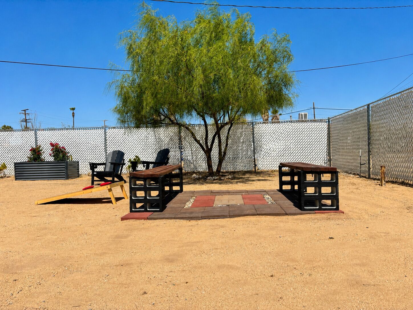 An outdoor patio area with a wooden bench, a small table, and a tree.