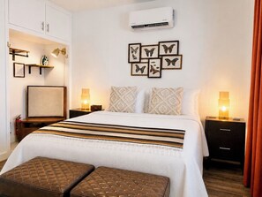 A hotel room with a bed, bedside tables, a wall-mounted air conditioner, and framed butterfly artwork.