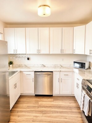 A kitchen with white cabinets, a stainless steel dishwasher, a microwave, and a stove.