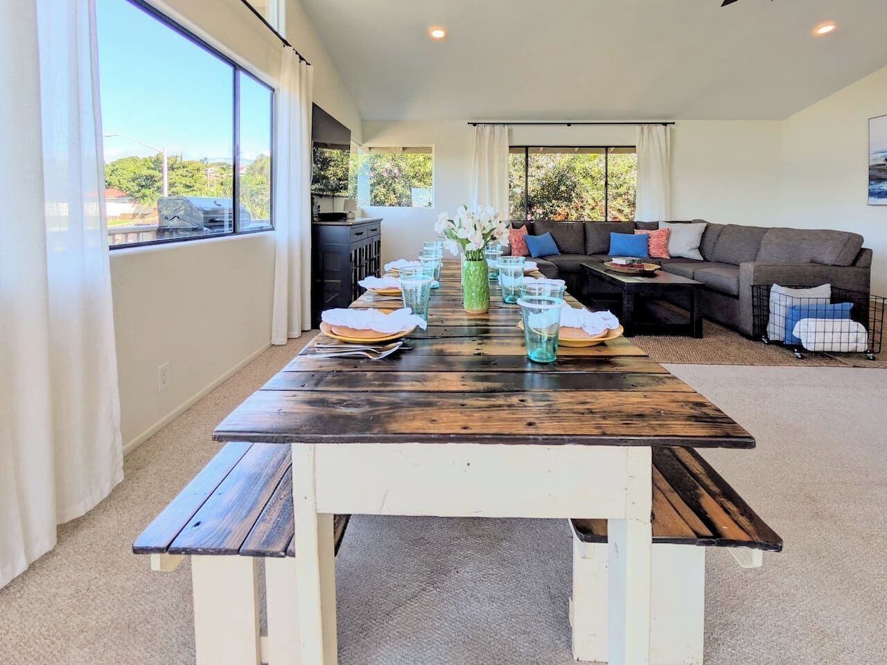 A dining area with a wooden table set for four, a sofa, and a view of greenery outside.