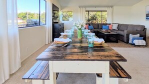 A dining area with a wooden table set for four, a sofa, and a view of greenery outside.