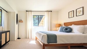 A bedroom with a bed, a bedside table, a lamp, and a window with curtains.