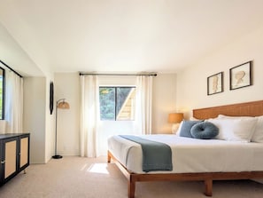 A bedroom with a bed, a bedside table, a lamp, and a window with curtains.