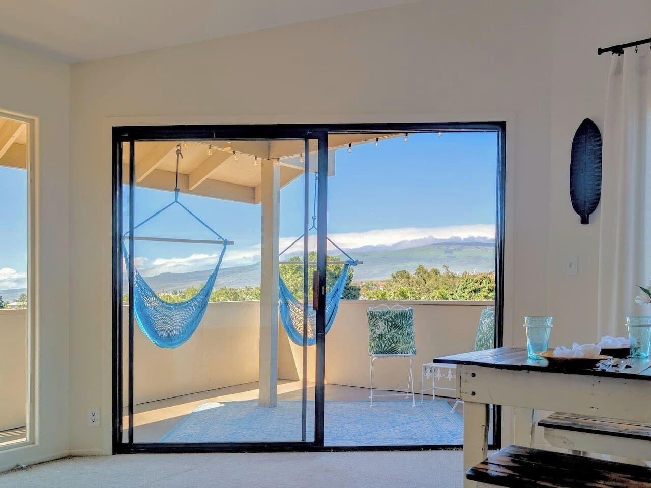 Un balcón con una hamaca, una mesa con vasos y vistas del paisaje.