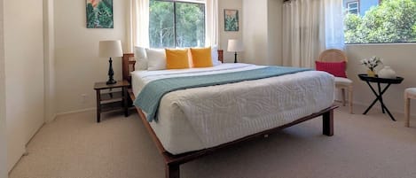 Un dormitorio con una cama grande, dos mesitas de noche, una silla y una ventana con cortinas.