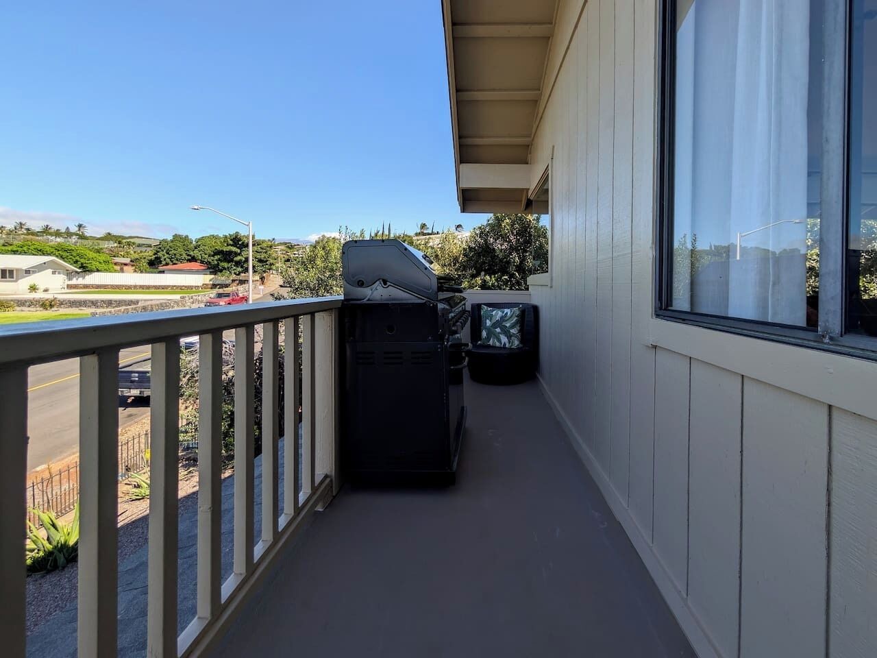 Un balcon avec un barbecue, une poubelle et une vue sur une route et des espaces verts.