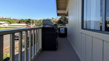 Un balcon avec un barbecue, une poubelle et une vue sur une route et des espaces verts.
