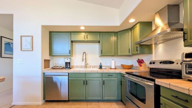 A kitchen with green cabinets, stainless steel appliances, and a tiled backsplash.