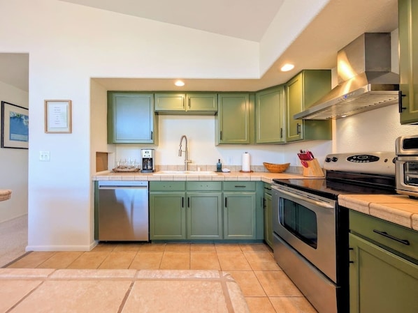 A kitchen with green cabinets, stainless steel appliances, and a tiled backsplash.