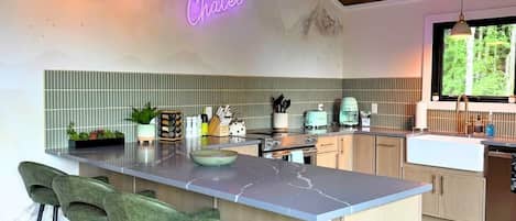 A modern kitchen with a bar area, wooden ceiling, and a neon sign.