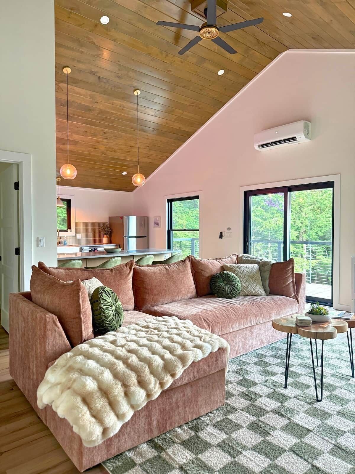 Uma sala de estar ampla com um sofá seccional rosa grande, um cobertor branco e um ventilador de teto.