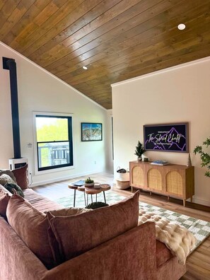 Ein modernes Wohnzimmer mit einem großen Fenster, einem Sofa, einem Couchtisch und einem Fernseher auf einem Schrank.