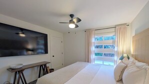 A bedroom with a bed, a ceiling fan, a TV, a window with curtains, a bedside table, and a lamp. - Hale Maluhia, Newly renovated, 1BR, sleeps 3. (Waikoloa Village)