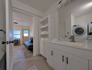 A modern bathroom with a large mirror, white cabinetry, and a built-in washing machine.