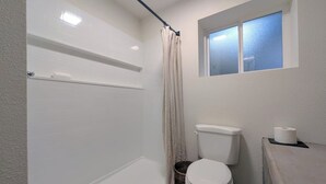A bathroom with a bathtub, toilet, and a window above the toilet. - Hale Maluhia, Newly renovated, 1BR, sleeps 3. (Waikoloa Village)