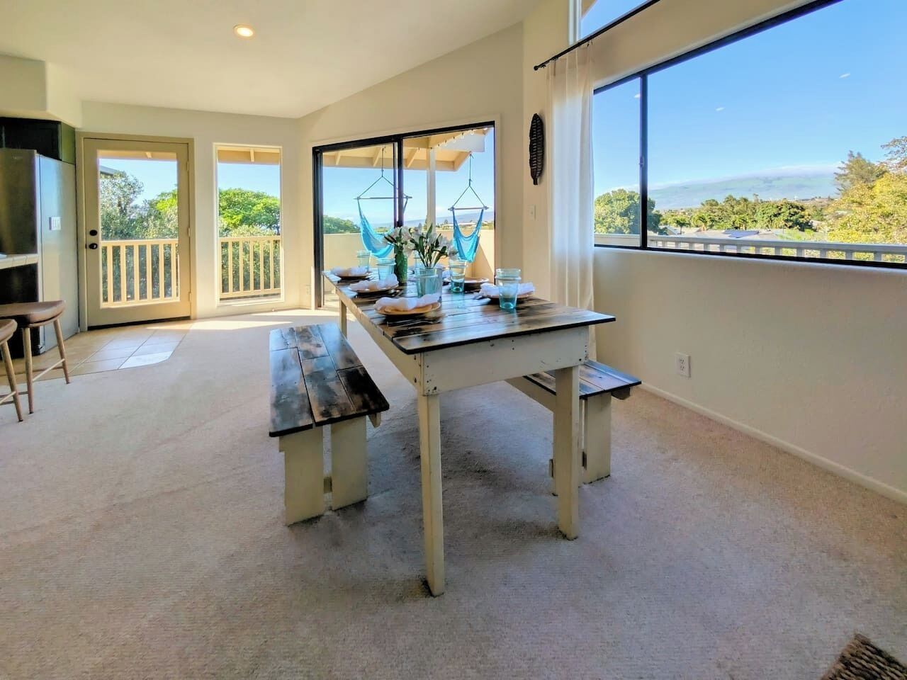 A room with a large window, a table with chairs, and a view of greenery outside.