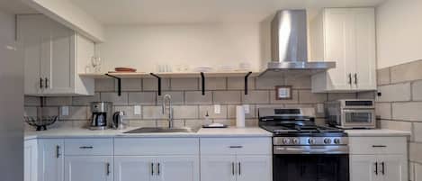 Una cocina moderna con armarios blancos, estufa de acero inoxidable y microondas.