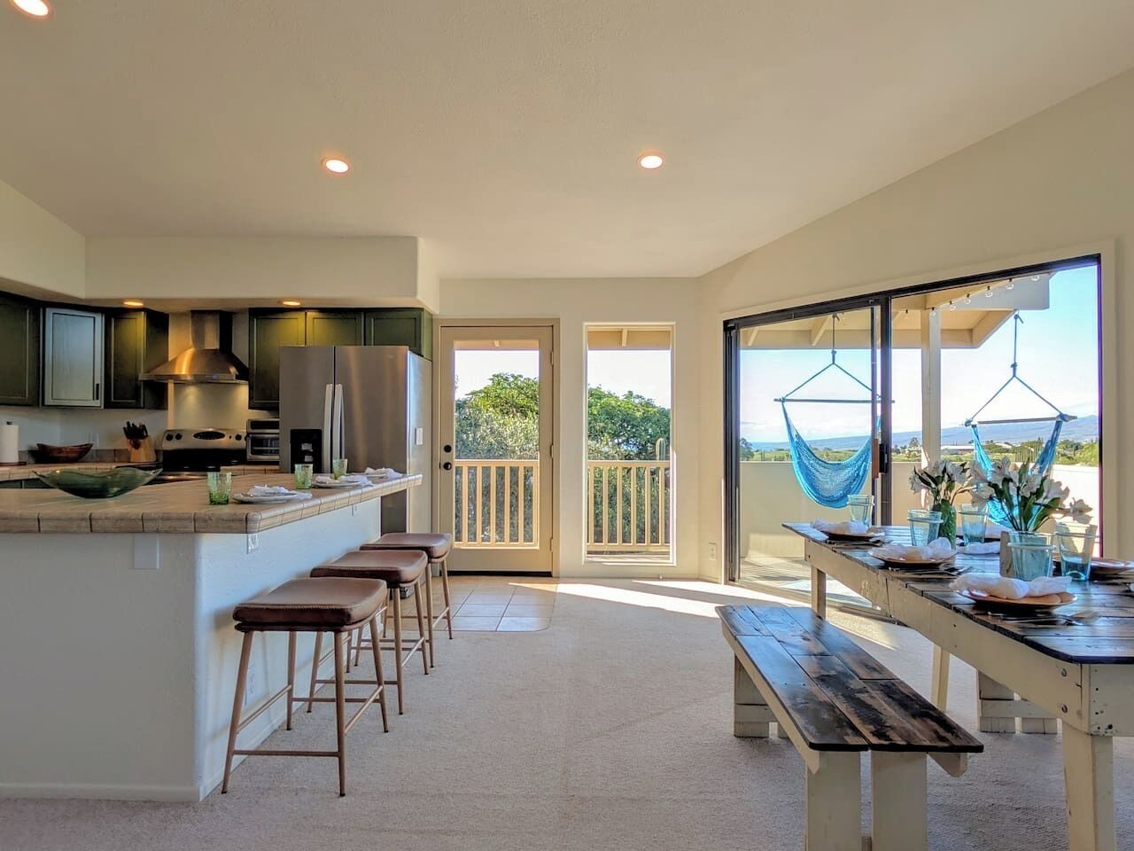 A modern kitchen with a bar area, a dining table set for two, and a balcony with a view.
