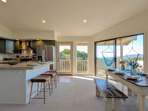 A modern kitchen with a bar area, a dining table set for two, and a balcony with a view. - Hale Mauna, Waikoloa 1 House, 2 Units. (Waikoloa Village)