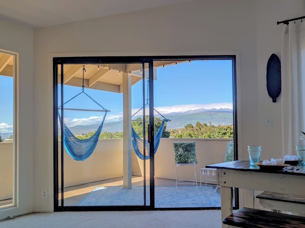 Un balcon avec un hamac, une chaise et une table sur laquelle se trouvent des verres et une assiette.