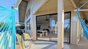 Une terrasse couverte avec un hamac, du mobilier d’extérieur et une porte-fenêtre coulissante donnant sur un espace de repas intérieur.