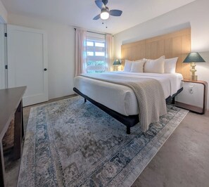 A bedroom with a bed, bedside lamps, a ceiling fan, a window with curtains, and a rug. - Hale Mauna, Waikoloa 1 House, 2 Units. (Waikoloa Village)