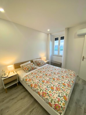 Un dormitorio con cama, mesitas de noche, una ventana y un equipo de aire acondicionado.