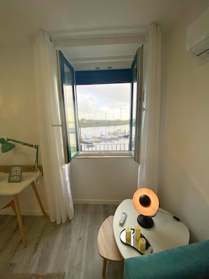 Una habitación con vistas a barcos en un puerto deportivo, un escritorio con lámpara y una cama con cubrecama azul.