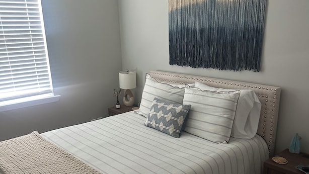 Quarto com cama, mesa de cabeceira, obra de arte na parede e janela com persianas.