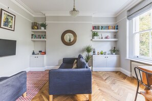 A living room with a sofa, a coffee table, a fireplace, and a bookshelf. - Stylish North Kensington One-Bed (London)
